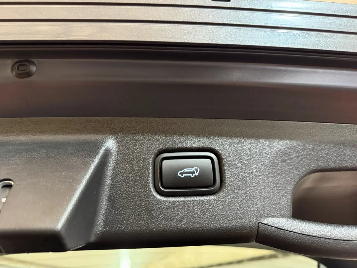 Gros plan sur le bouton d'ouverture électrique du coffre du Hyundai Tucson gris foncé, intérieur du hayon visible.