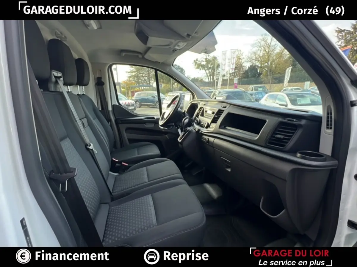 Vue intérieure côté passager du Ford Transit Custom blanc, montrant les sièges et le tableau de bord noir.