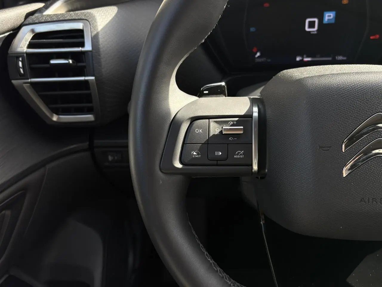 Gros plan sur le volant cuir noir du Citroën C5 X 2024, avec commandes multifonctions côté gauche et tableau de bord numérique.