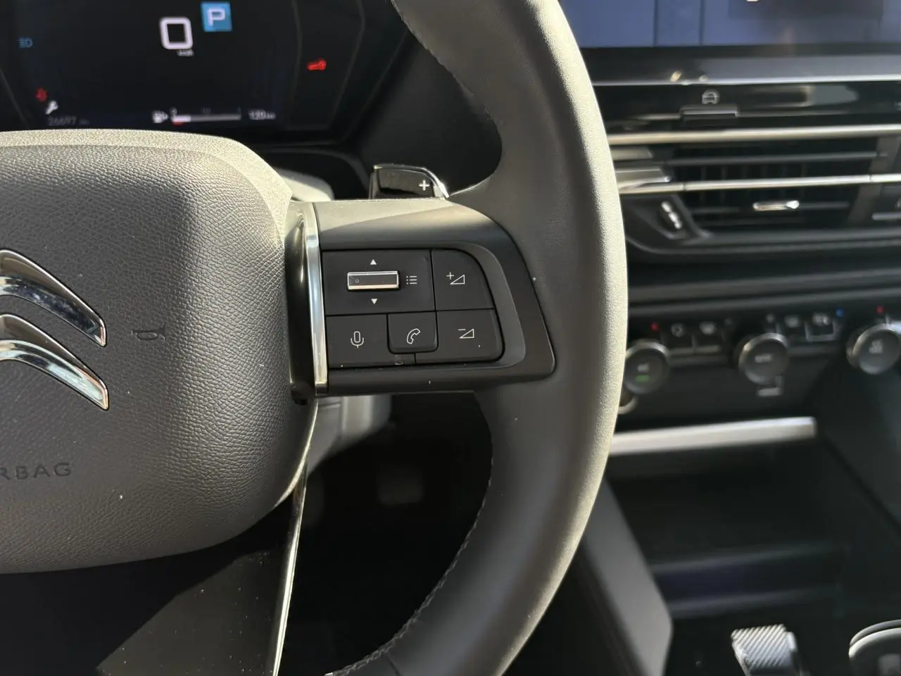 Gros plan sur le volant cuir noir du Citroën C5 X 2024 avec commandes audio et tableau de bord numérique en arrière-plan.