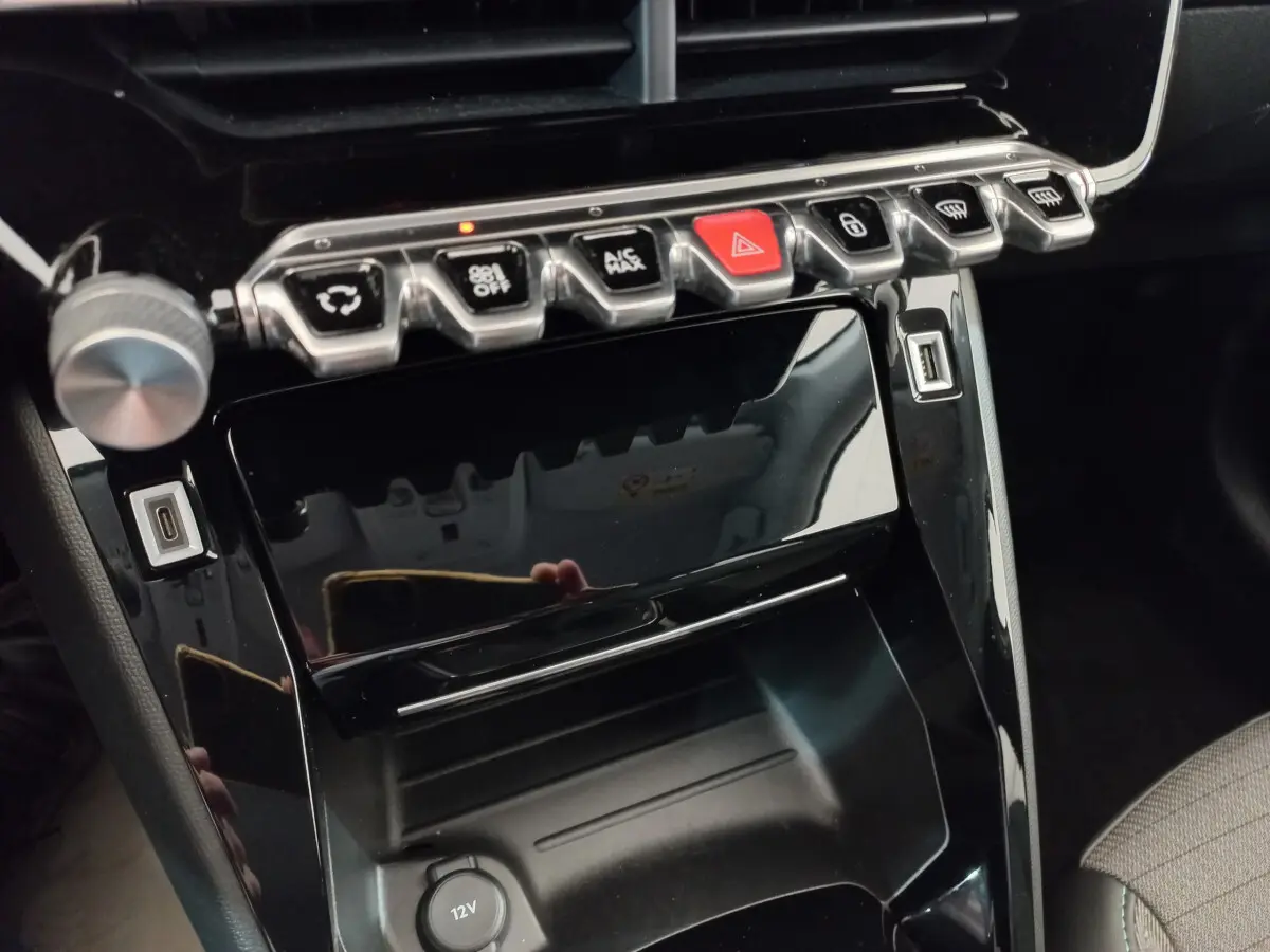 Gros plan sur la console centrale noire brillante de la Peugeot 208 PureTech 100 S&S Allure avec boutons de commande et ports USB.