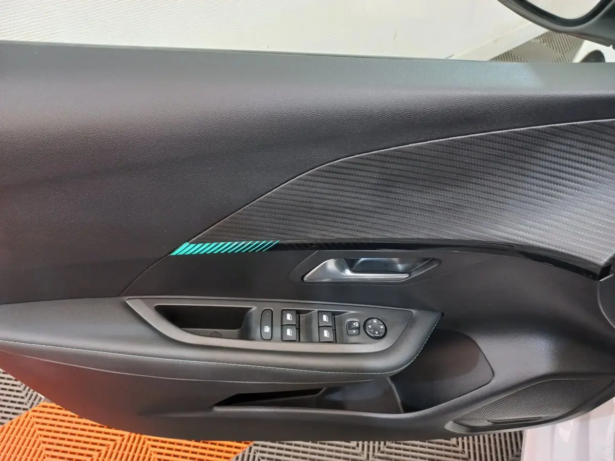 Vue intérieure du panneau de porte côté conducteur de la Peugeot 208 blanc, avec commandes électriques et insert décoratif noir à motif carbone.