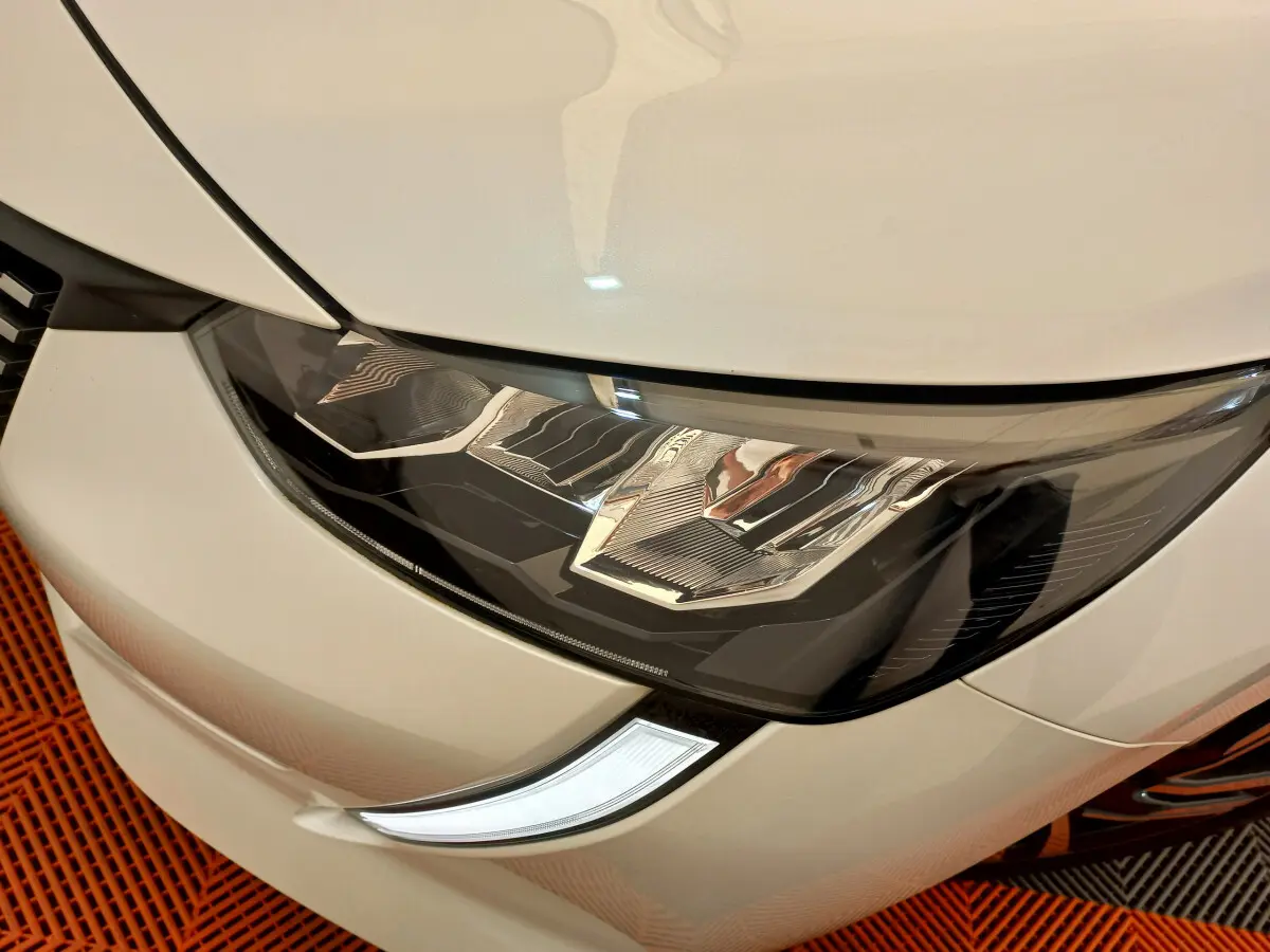 Gros plan sur le phare avant droit de la Peugeot 208 blanche, mettant en valeur son design LED distinctif.
