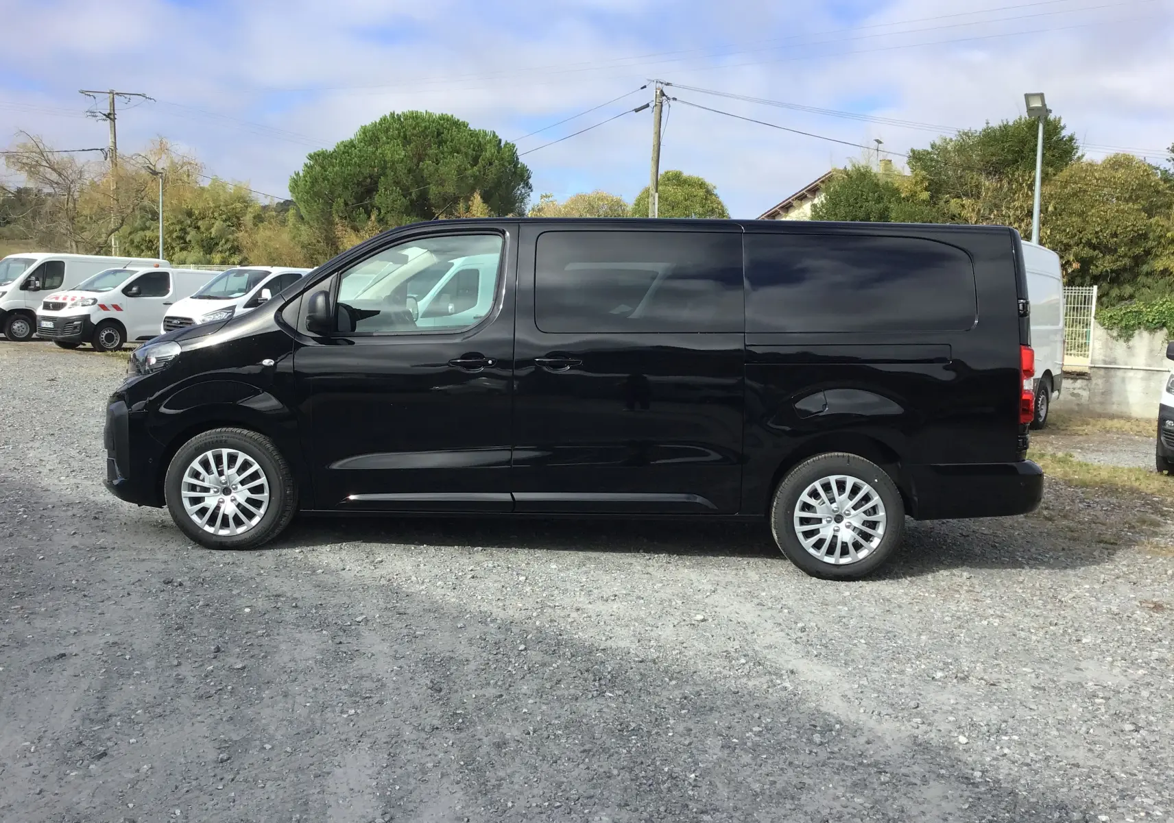 Profil côté gauche d’un Peugeot Expert cabine approfondie noir, avec jantes alliage et vitres teintées, sur un parking extérieur.