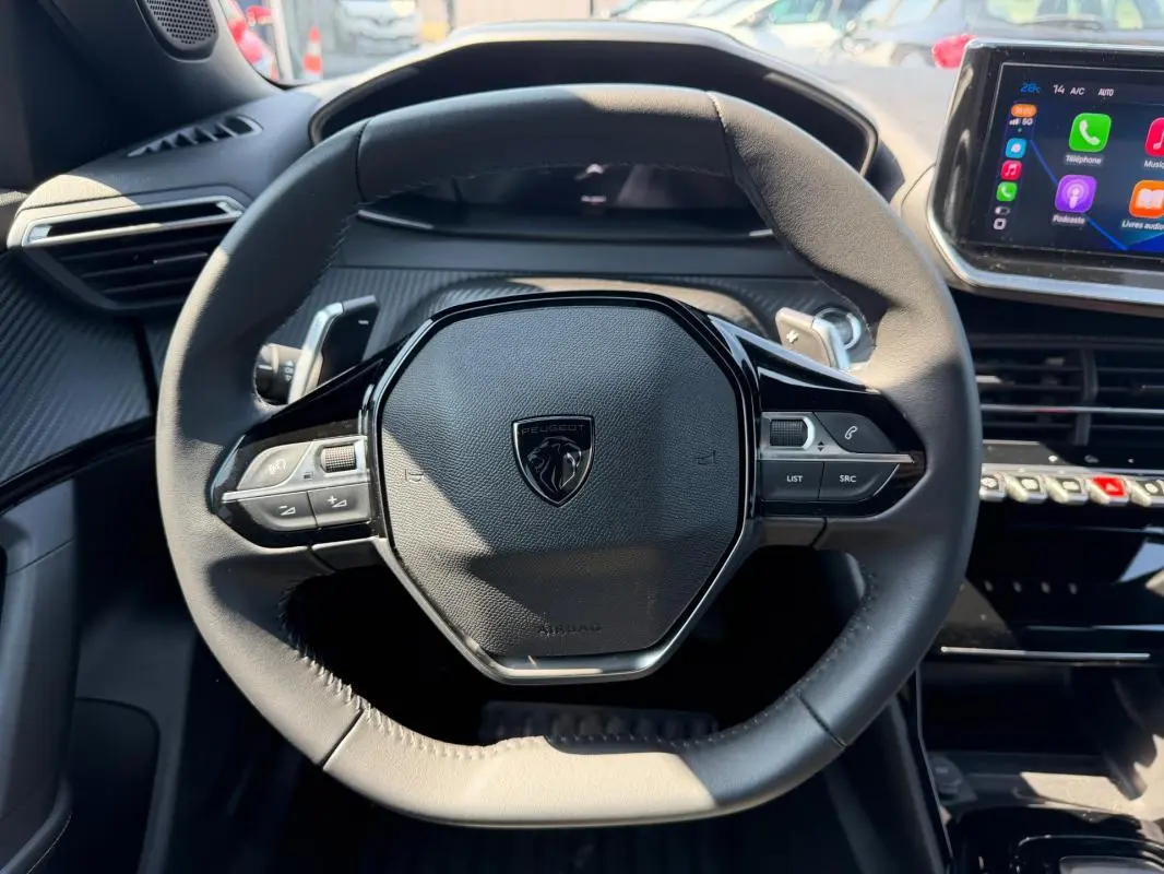 Vue rapprochée du volant noir du Peugeot 2008 Hybrid 145 e-DCS6 Allure 2025 avec tableau de bord et écran tactile visible.