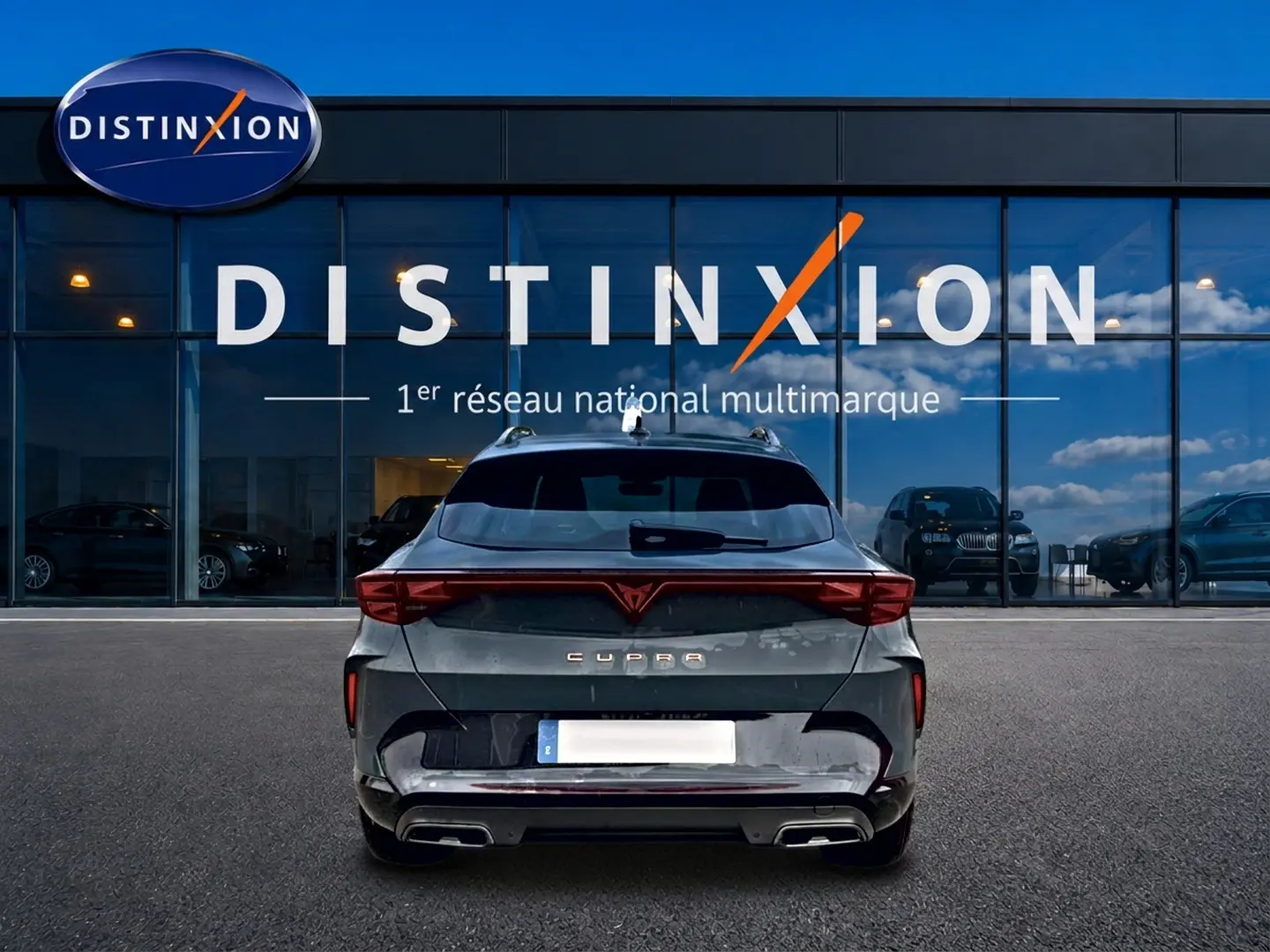 Vue arrière d'une CUPRA Formentor bleu fjord 2026 avec feux LED et double sortie d'échappement, devant un showroom Distinxion.