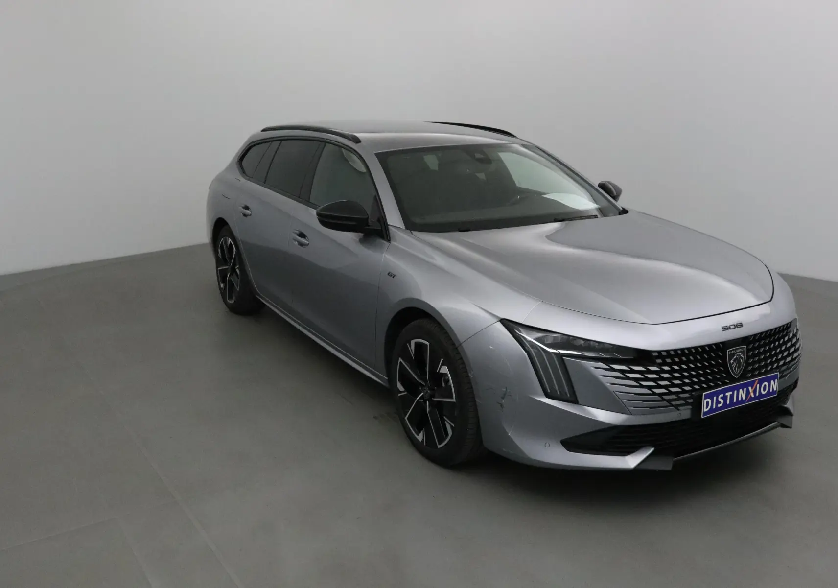 Peugeot 508 SW gris Artense en 3/4 avant droit, avec calandre distinctive et jantes noires stylées.