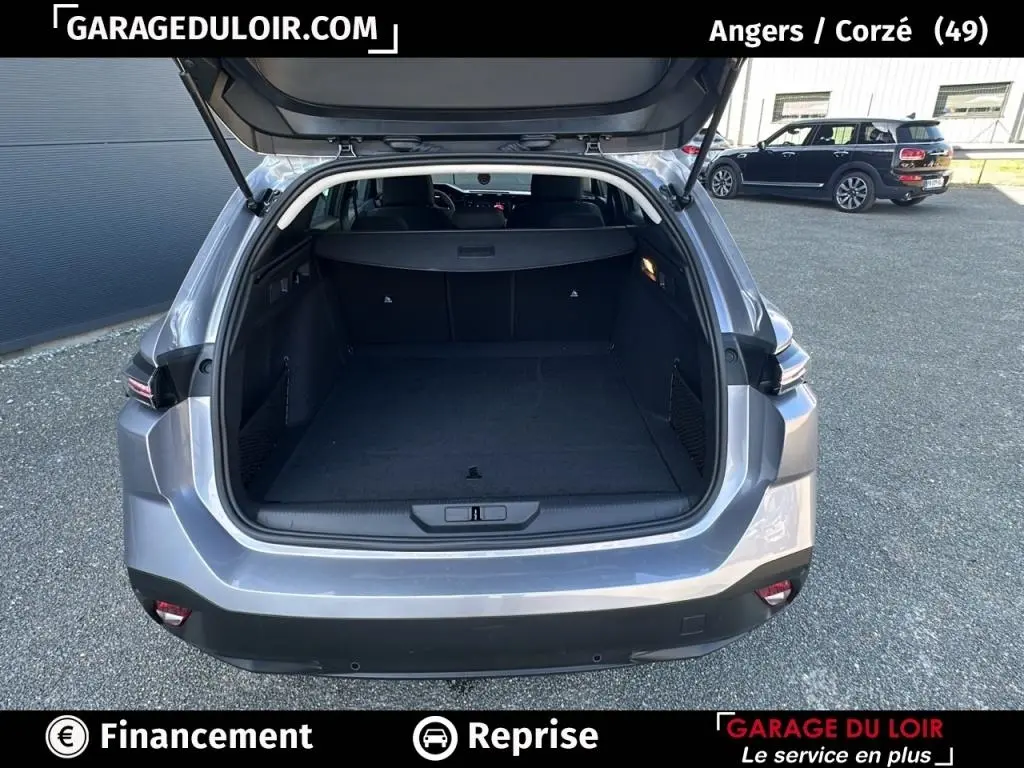 Coffre ouvert vu de l'arrière d'une Peugeot 308 gris clair 2023, montrant l'espace de chargement vide.