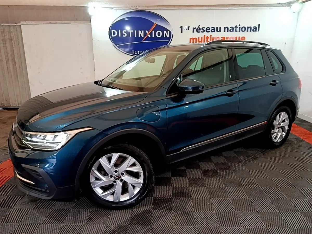 Vue 3/4 avant droit d'un Volkswagen Tiguan bleu hybride rechargeable, avec jantes alliage et prises de recharge visibles.