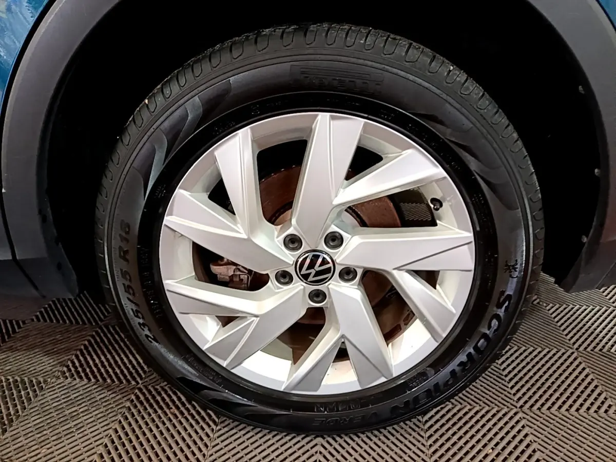 Gros plan sur la roue avant droite du Volkswagen Tiguan bleu, avec jante alliage argentée et logo VW central.
