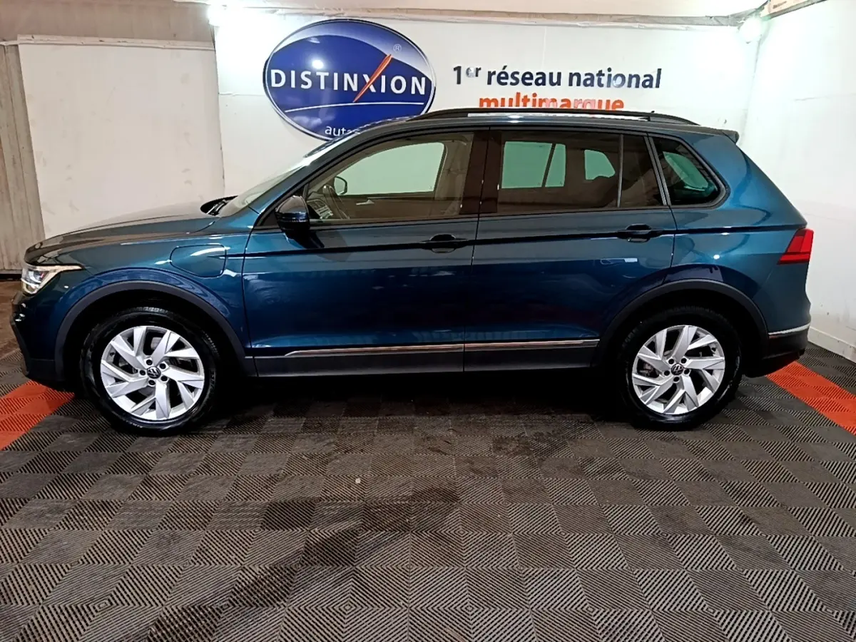 Vue latérale droite d'un Volkswagen Tiguan bleu hybride rechargeable, avec jantes alliage et prise de recharge visible sur l'aile avant.