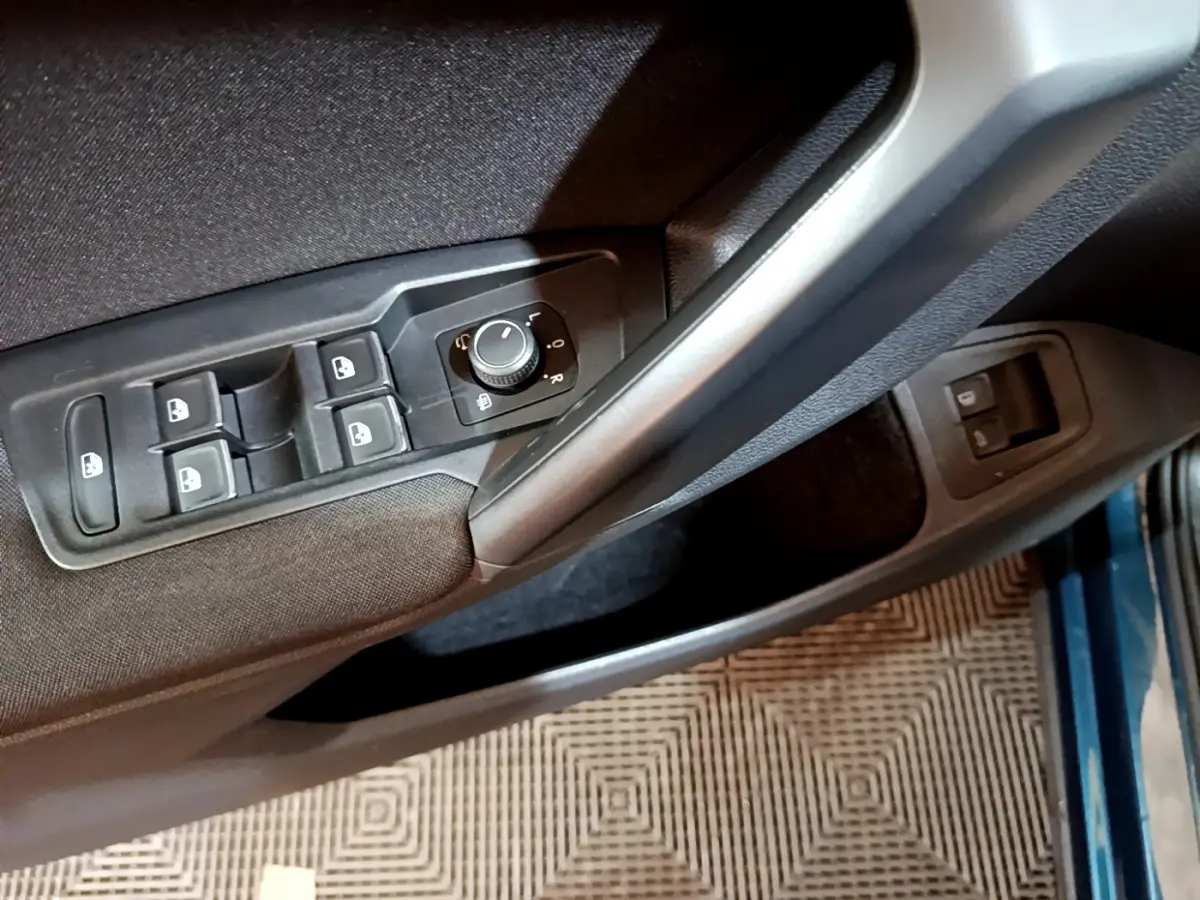 Vue rapprochée du panneau de commandes des vitres et rétroviseurs côté conducteur d’un Volkswagen Tiguan bleu.