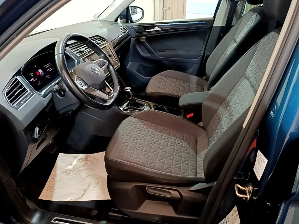 Intérieur du Volkswagen Tiguan bleu 2021, vue côté conducteur, volant cuir et sièges tissu gris à motifs géométriques.