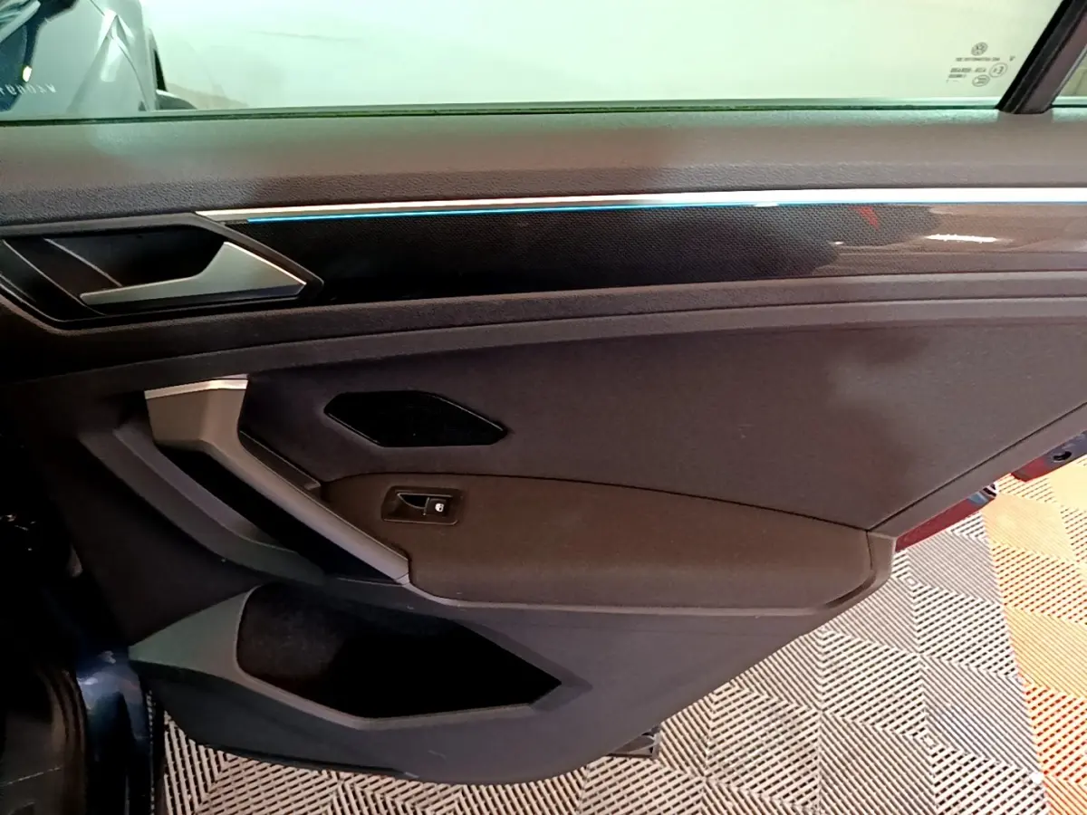 Intérieur de la porte avant gauche du Volkswagen Tiguan bleu, avec poignée argentée et bande lumineuse fine.