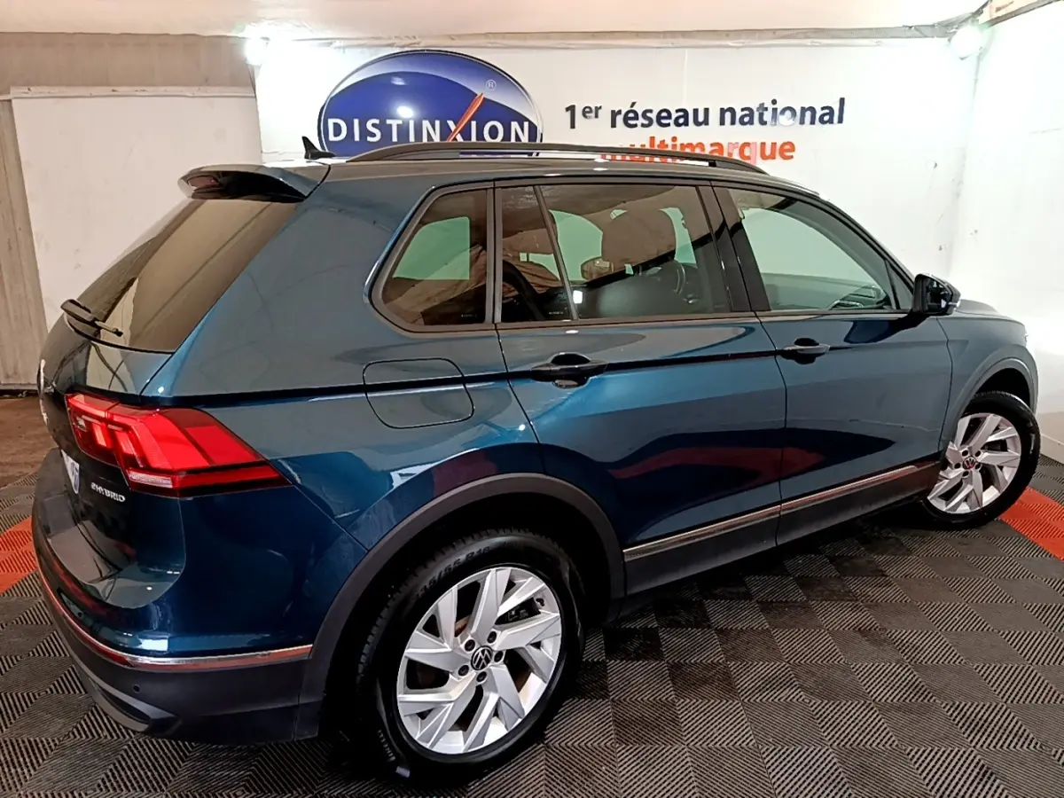 Vue 3/4 arrière droite d'un Volkswagen Tiguan bleu hybride rechargeable avec jantes alliage et vitres teintées.