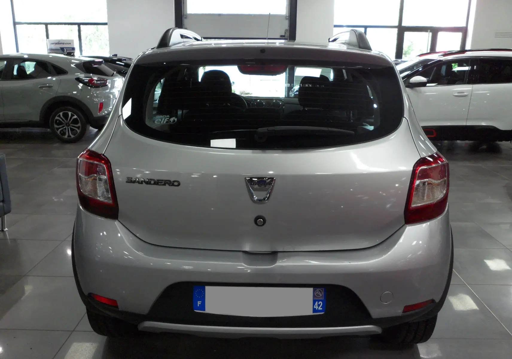 Vue arrière d'une Dacia Sandero Stepway gris platine 2016 en intérieur, avec logo et feux arrière visibles.