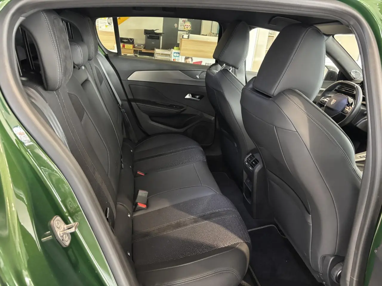 Vue intérieure arrière côté gauche d’une Peugeot 308 GT 2024 vert, montrant la banquette et les sièges avant en sellerie tri matières noire.