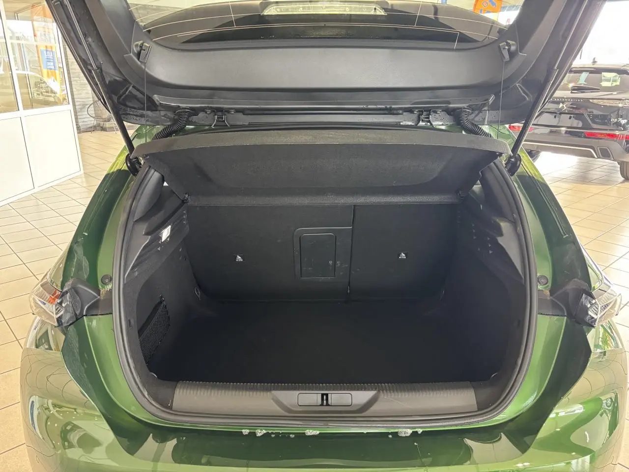 Coffre ouvert vu de l'arrière d'une Peugeot 308 GT berline 2024 vert métallisé en showroom.