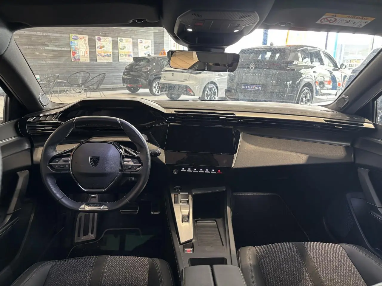Vue intérieure avant du Peugeot 308 2024 avec volant cuir, écran tactile central et sellerie tri-matières noire.