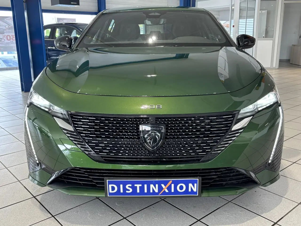 Vue frontale d'une Peugeot 308 berline GT 2024 vert métallisé avec calandre noire et feux LED griffés.