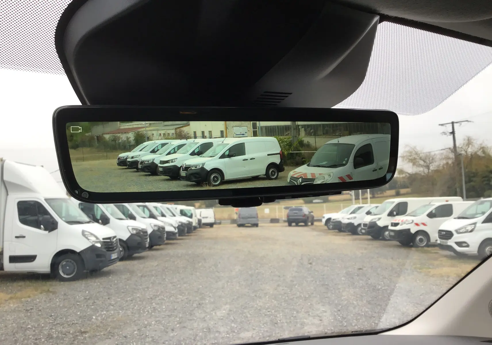 Vue intérieure du rétroviseur numérique montrant plusieurs utilitaires blancs en stationnement, avec un Peugeot Expert gris titane visible au premier plan.