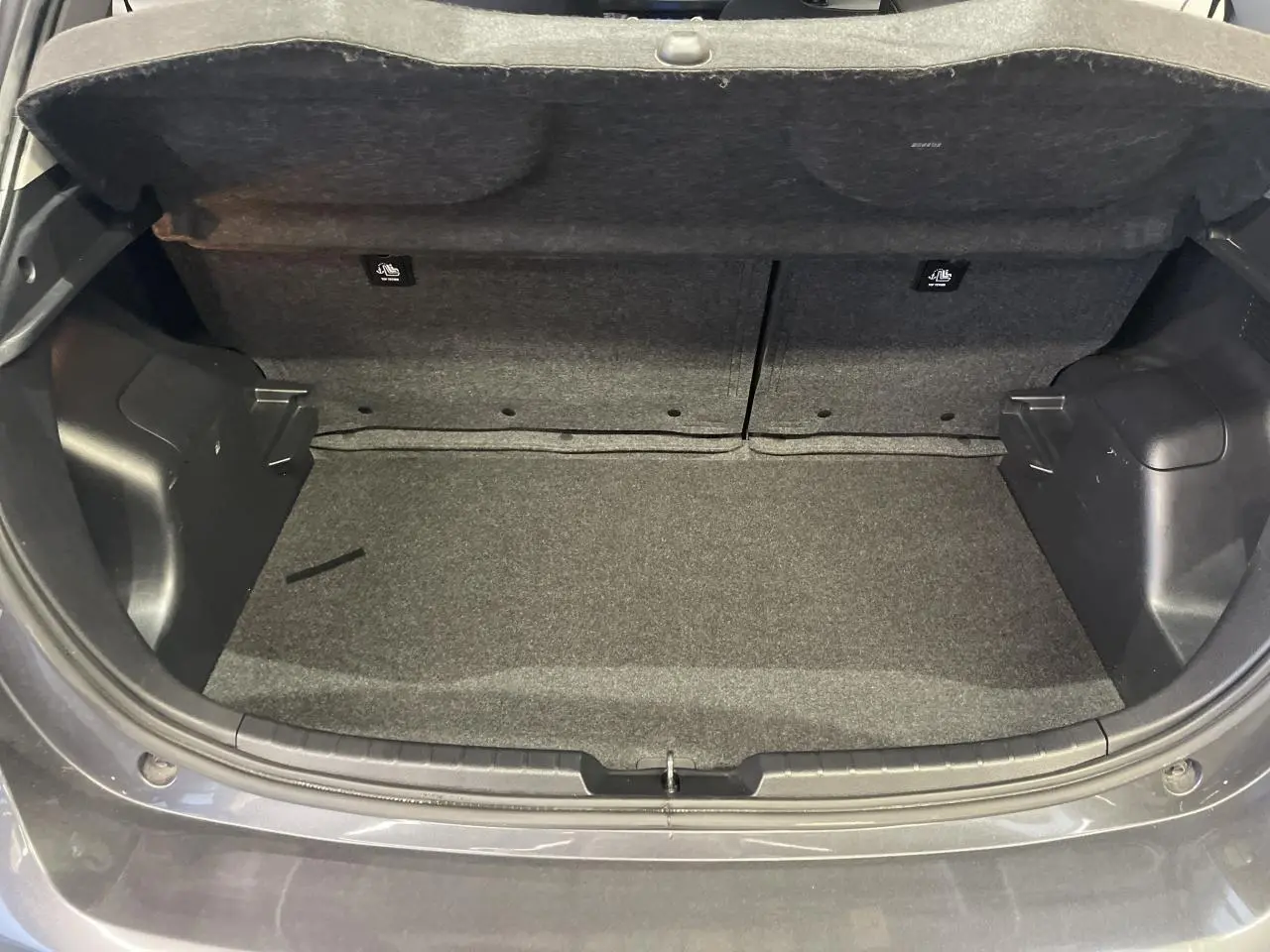 Coffre ouvert vu de l'arrière d'une Toyota Yaris hybride gris foncé métallisé, intérieur du coffre en tissu gris.