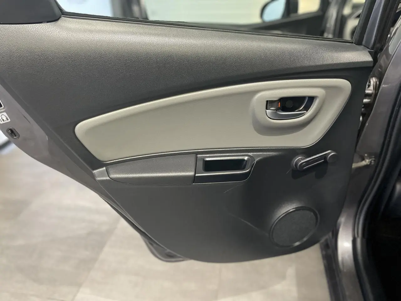 Vue rapprochée de la porte arrière droite gris foncé métallisé de la Toyota Yaris Hybride 2020 avec manivelle de vitre et poignée intérieure grise.