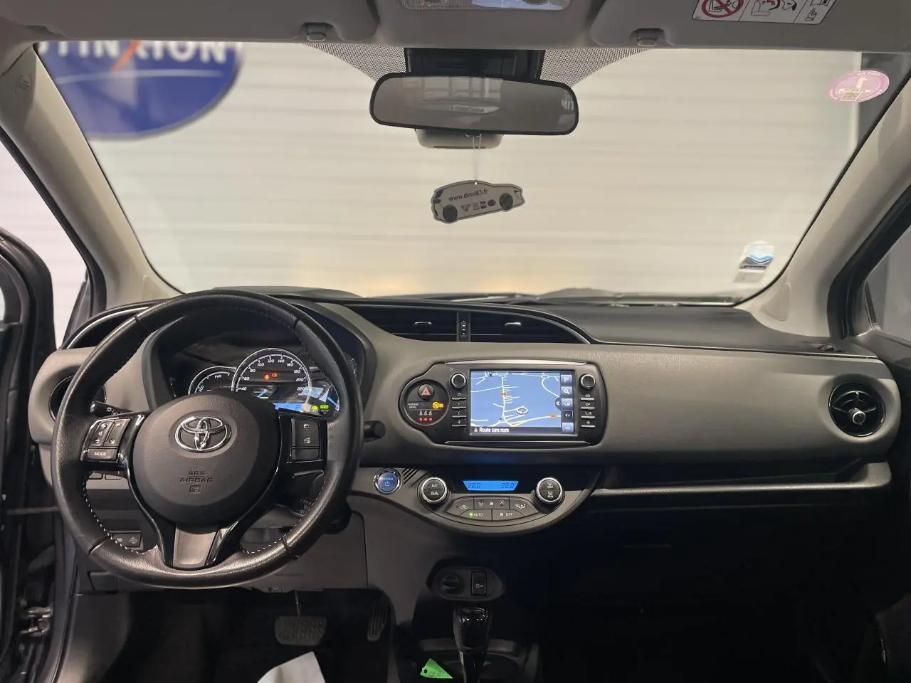 Vue frontale de l'intérieur de la Toyota Yaris hybride 2020 avec tableau de bord noir et écran tactile de navigation.
