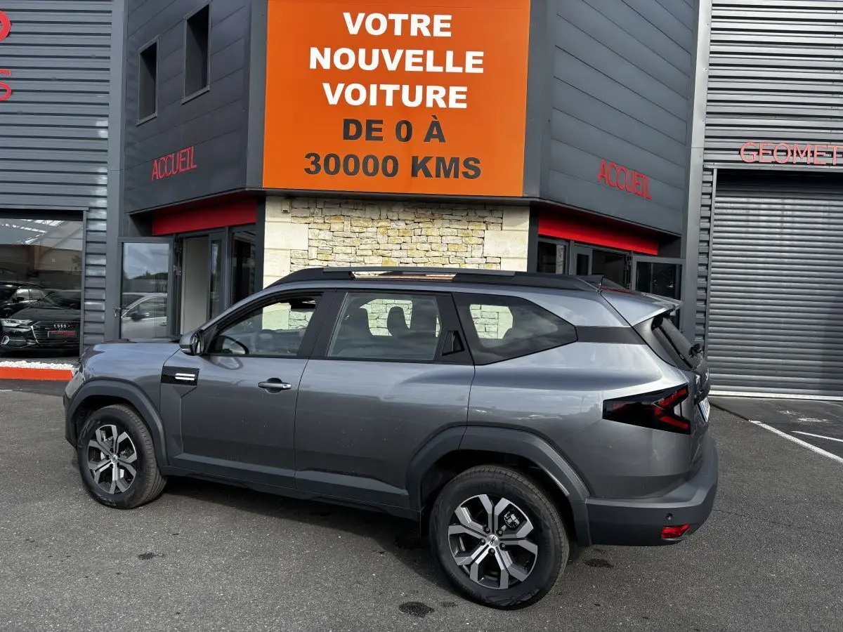 SUV Dacia Bigster gris foncé vu de profil côté gauche, avec barres de toit noires et feux arrière LED distinctifs.