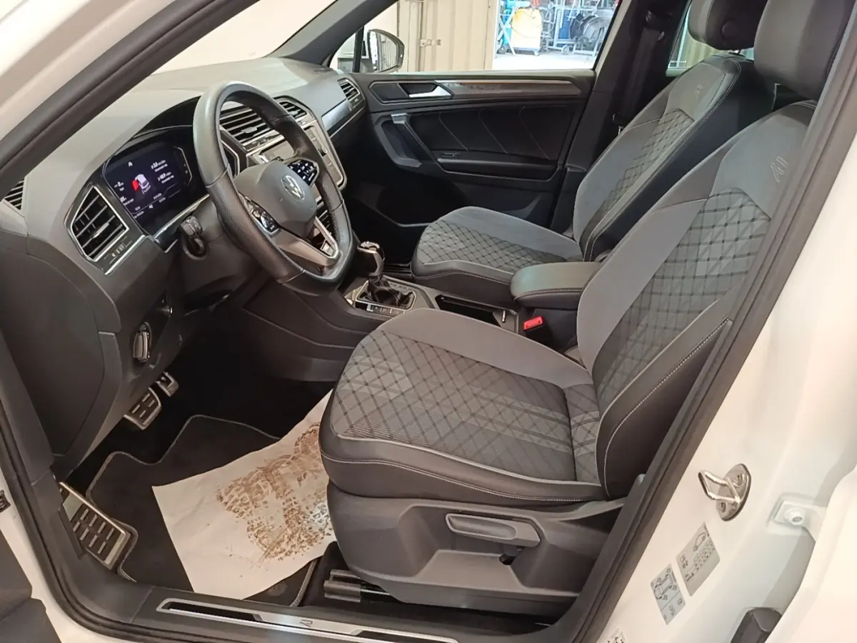 Vue intérieure côté conducteur du Volkswagen Tiguan blanc 2023, sièges R-Line avec surpiqûres et volant cuir multifonctions.