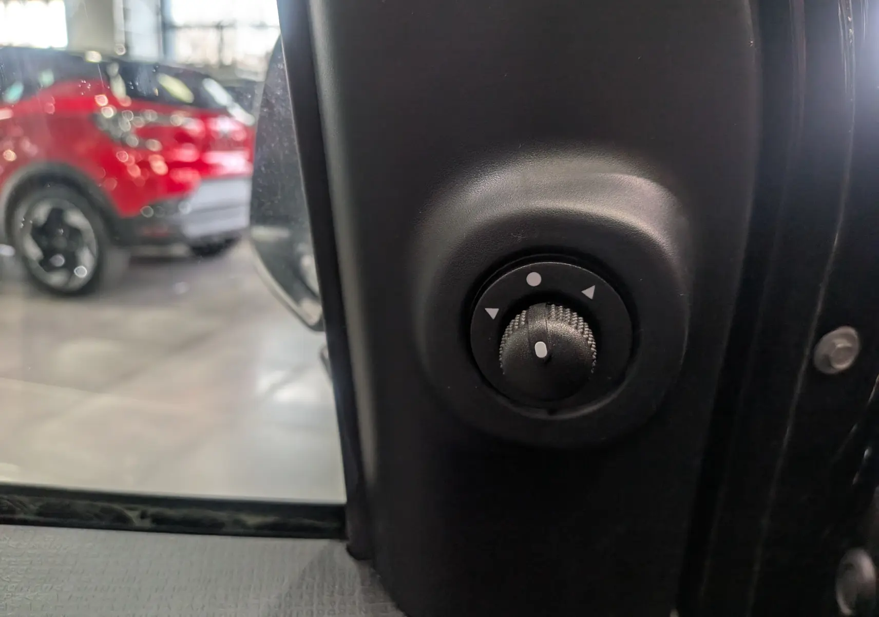 Gros plan sur le réglage des rétroviseurs électriques côté conducteur d'une Fiat Panda 2025 noir cinéma, intérieur visible.