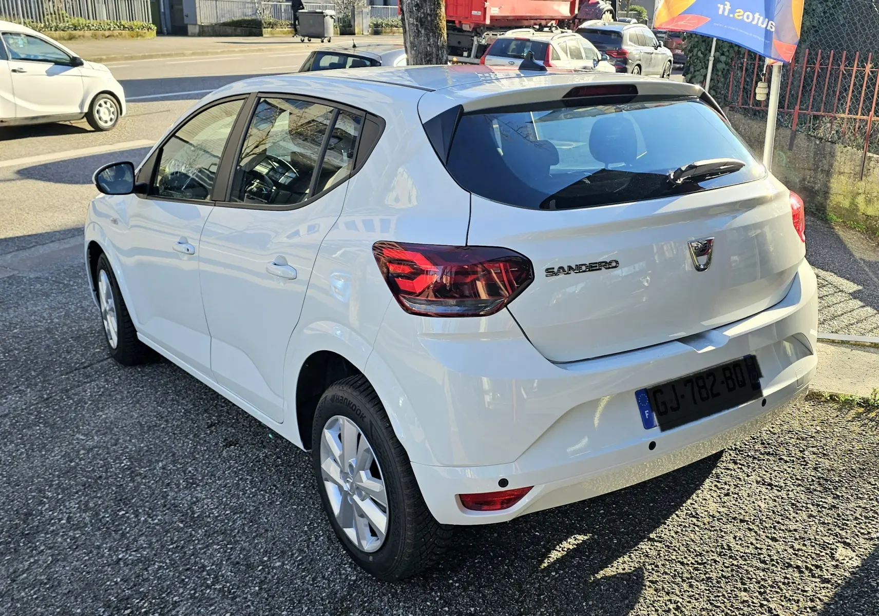 Vue 3/4 arrière droite d'une Dacia Sandero III blanche glacier avec feux arrière rouges et vitres teintées.