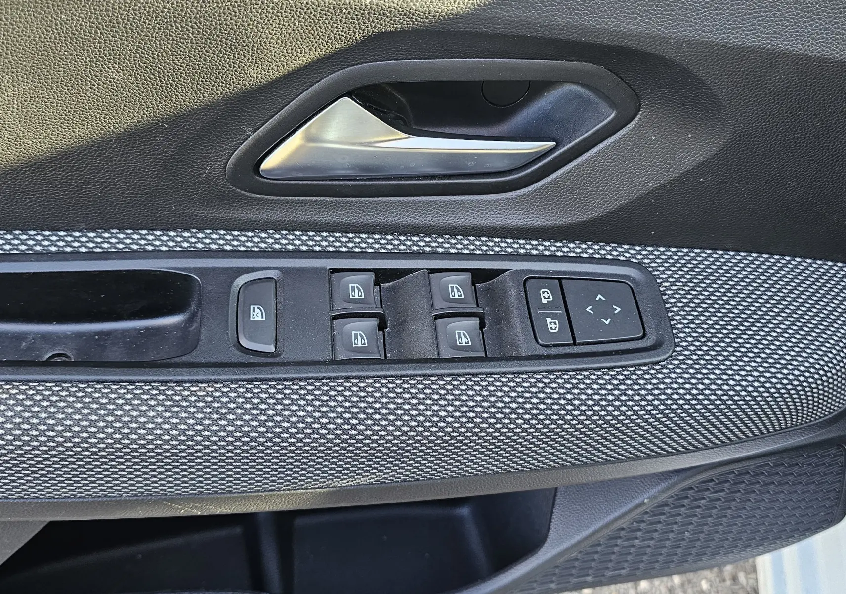 Gros plan sur la commande des vitres électriques et la poignée intérieure côté conducteur d’une Dacia Sandero III blanc glacier.