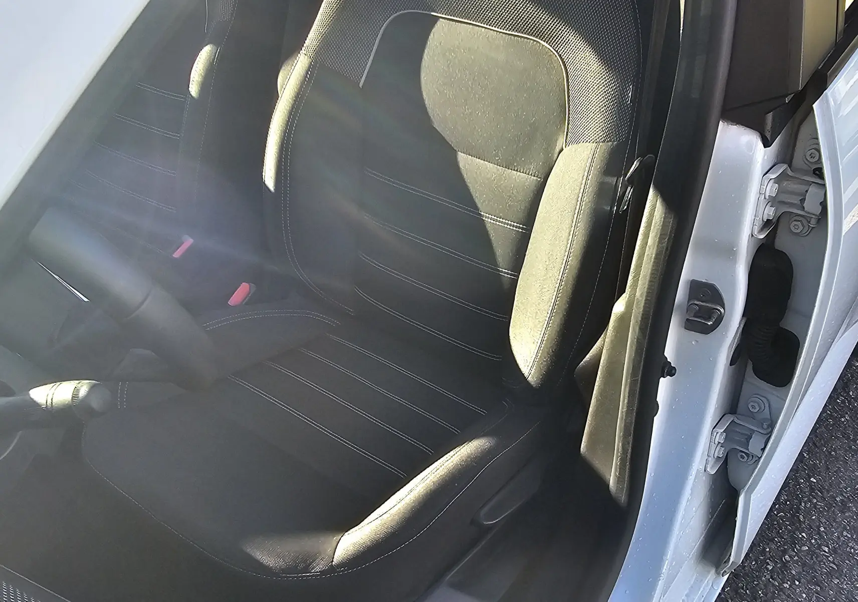 Vue intérieure côté conducteur de la Dacia Sandero III blanche, mettant en valeur le siège en tissu noir et la boîte manuelle.