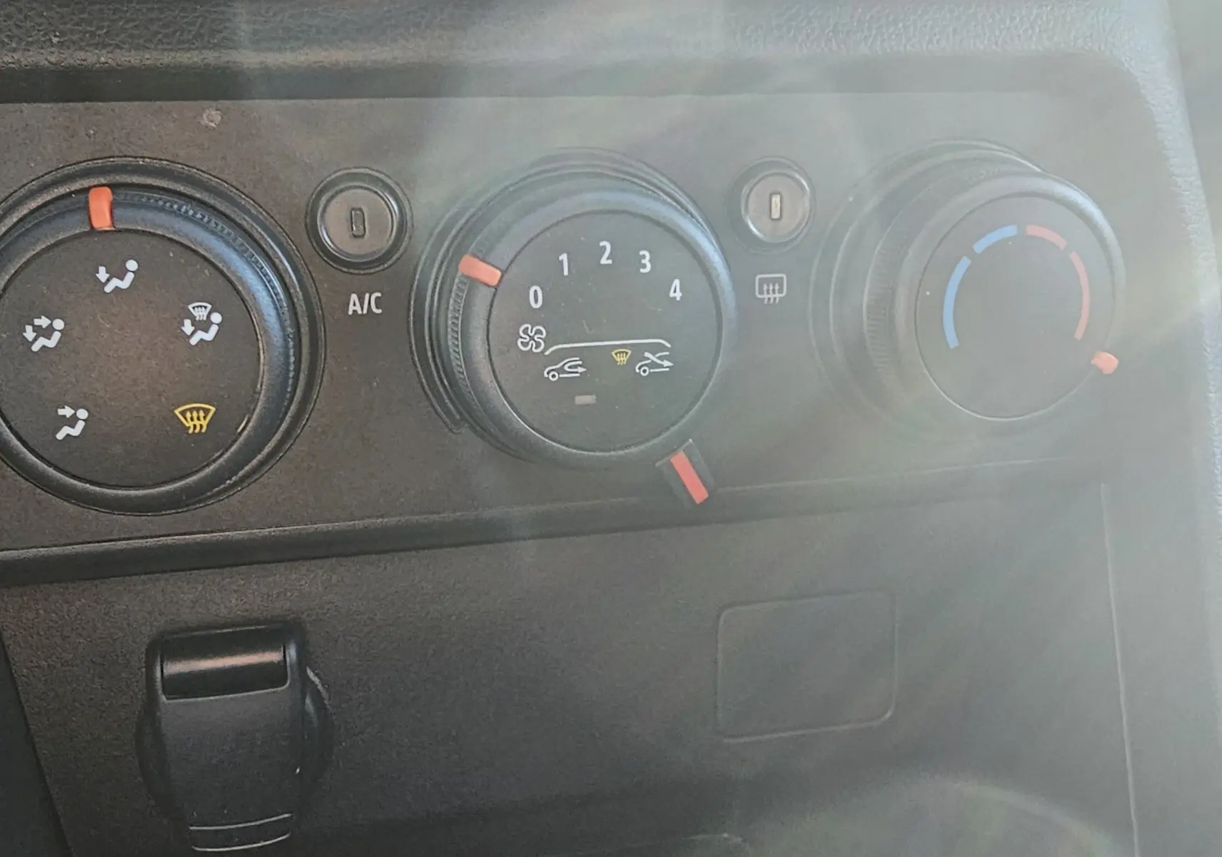 Gros plan sur les commandes de climatisation manuelle du tableau de bord d’une Dacia Sandero III blanche.