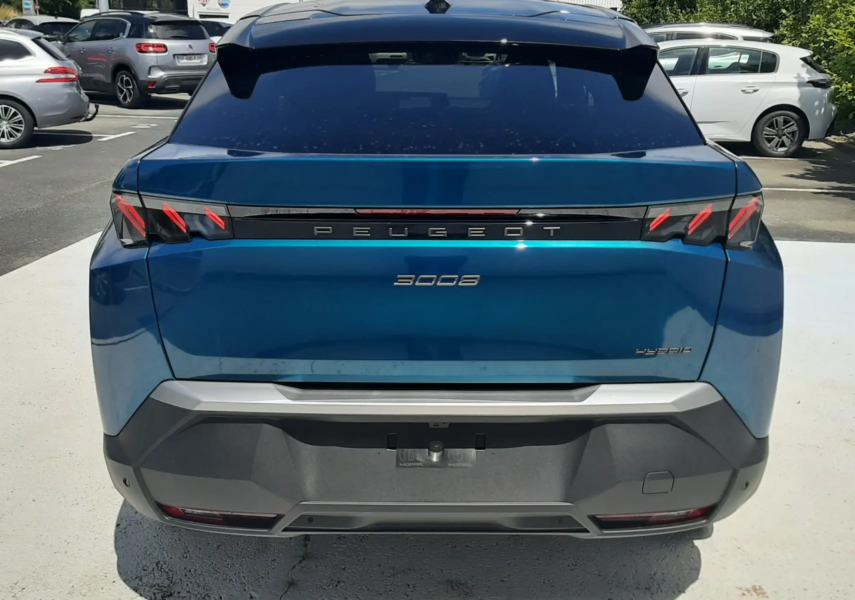 Vue arrière d'un Peugeot 3008 bleu obsession 2026 avec feux arrière à griffes rouges et logo hybride visible.
