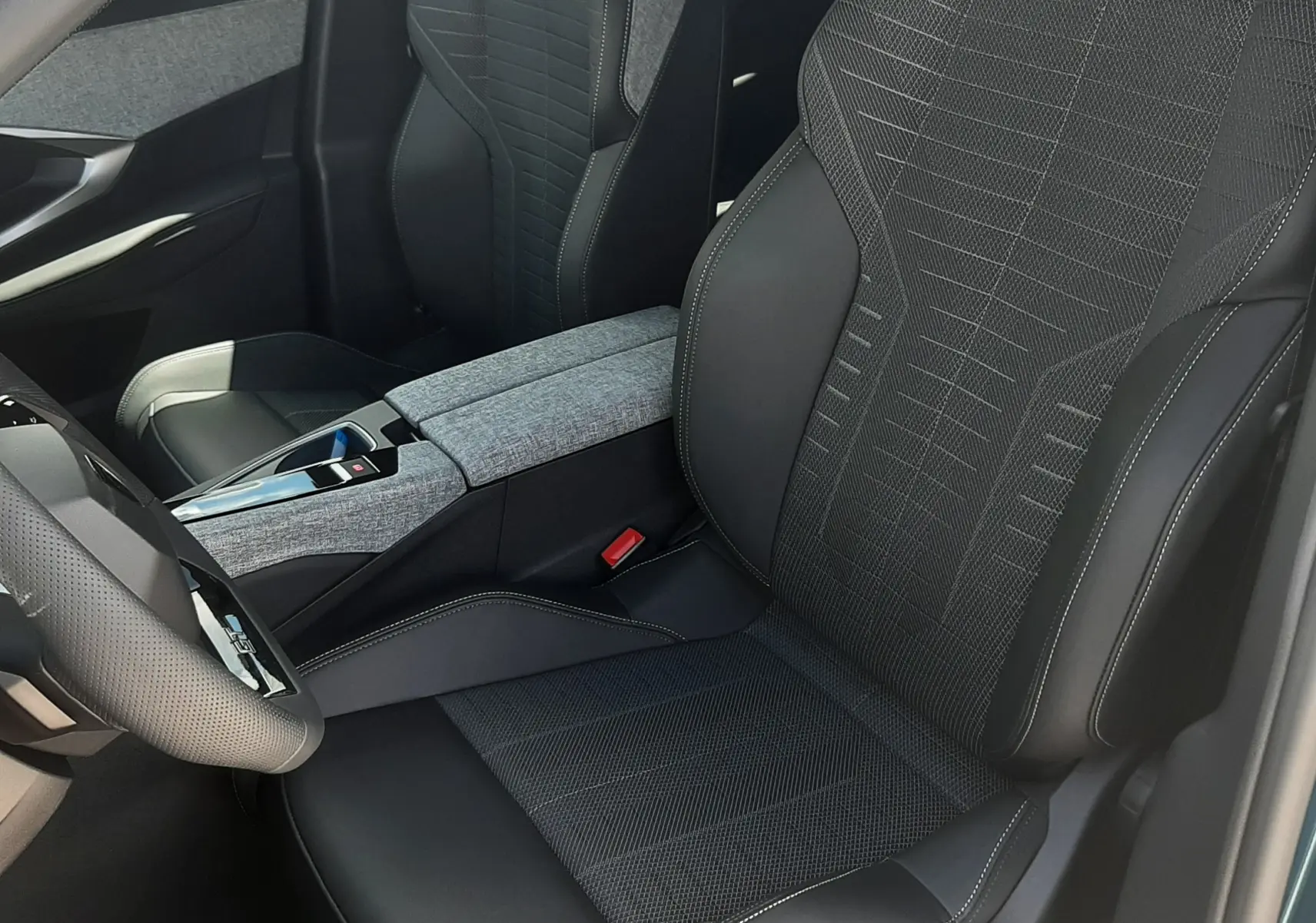 Vue intérieure côté conducteur du Peugeot 3008 1.2 Hybrid GT 2026, sièges noirs avec surpiqûres et console centrale grise.