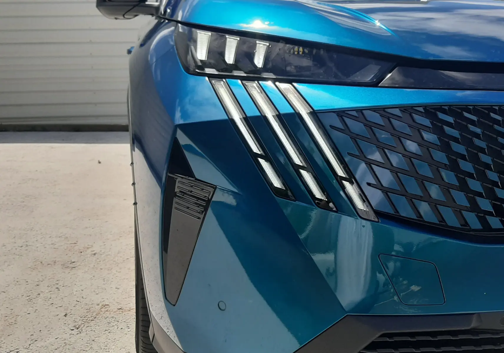 Vue avant gauche rapprochée du Peugeot 3008 1.2 Hybrid GT bleu obsession avec ses phares à griffes distinctifs.