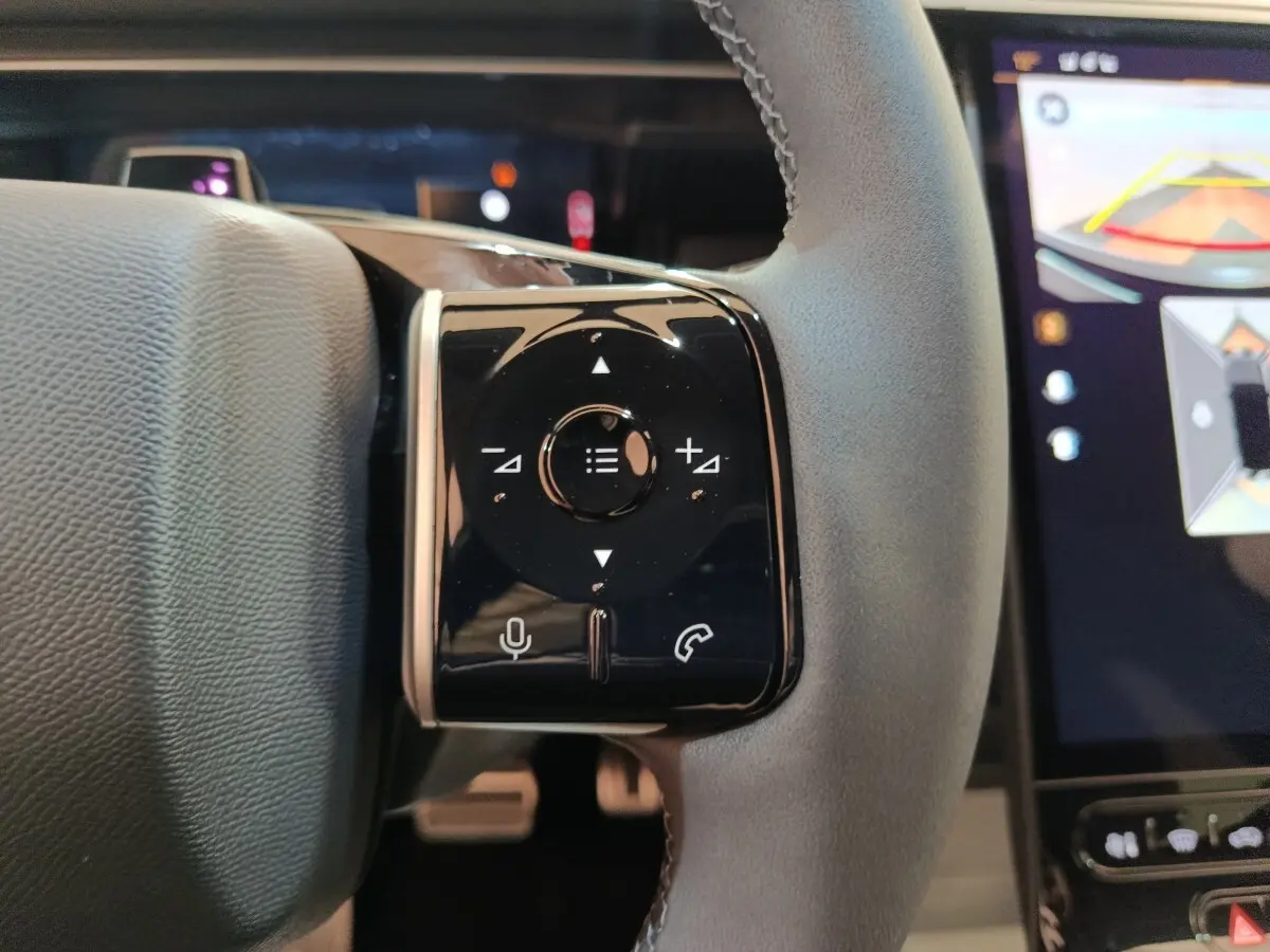 Gros plan sur les commandes tactiles noires du volant cuir gris du Citroën C5 hybride 2026, écran multifonctions visible.