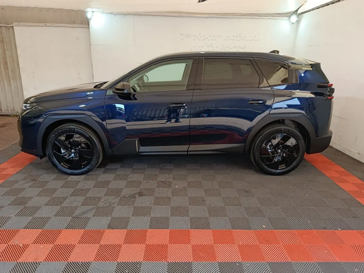 Vue latérale droite d'un Citroën C5 hybride bleu foncé avec jantes noires et toit noir dans un garage.