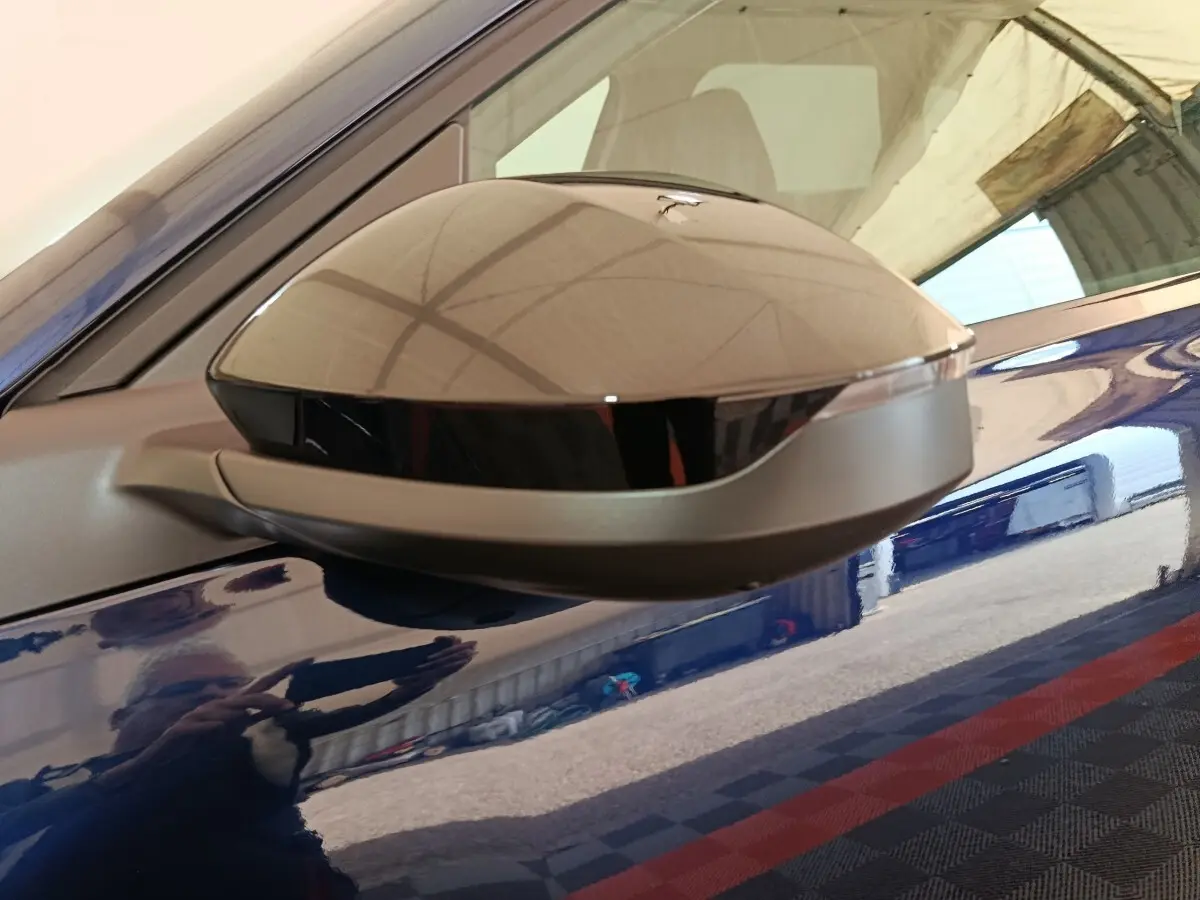 Gros plan sur le rétroviseur droit gris métallisé d'une Citroën C5 hybride bleu brillant, reflet de l'environnement visible.