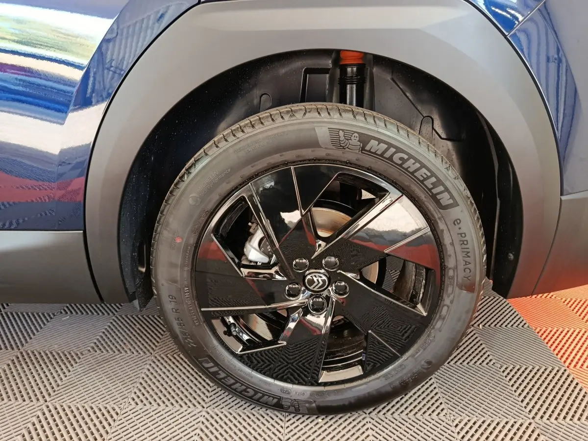 Gros plan sur la roue avant gauche noire brillante d'une Citroën C5 hybride bleue, avec pneu Michelin visible.