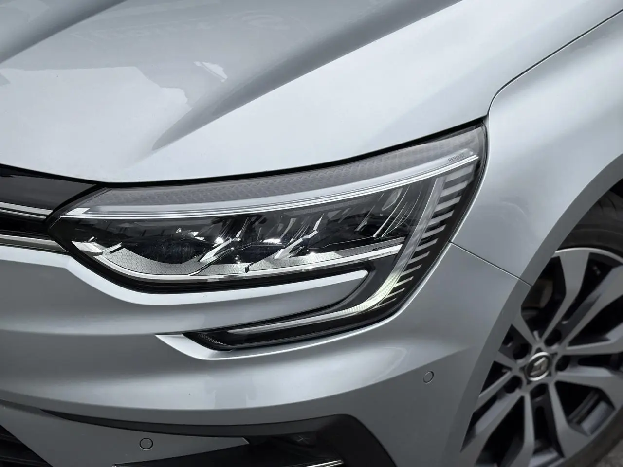 Gros plan sur le phare avant droit et la jante alliage gris d'une Renault Mégane Break 2024 gris Highland