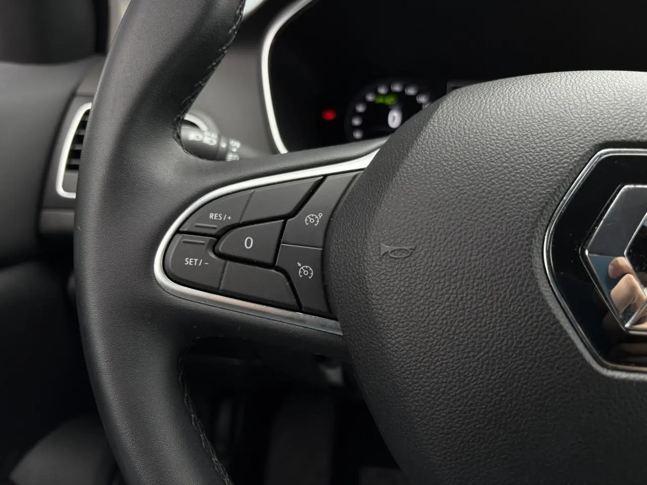 Gros plan sur le volant noir de la Renault Mégane Break 2024, avec commandes de régulateur de vitesse visibles à gauche.