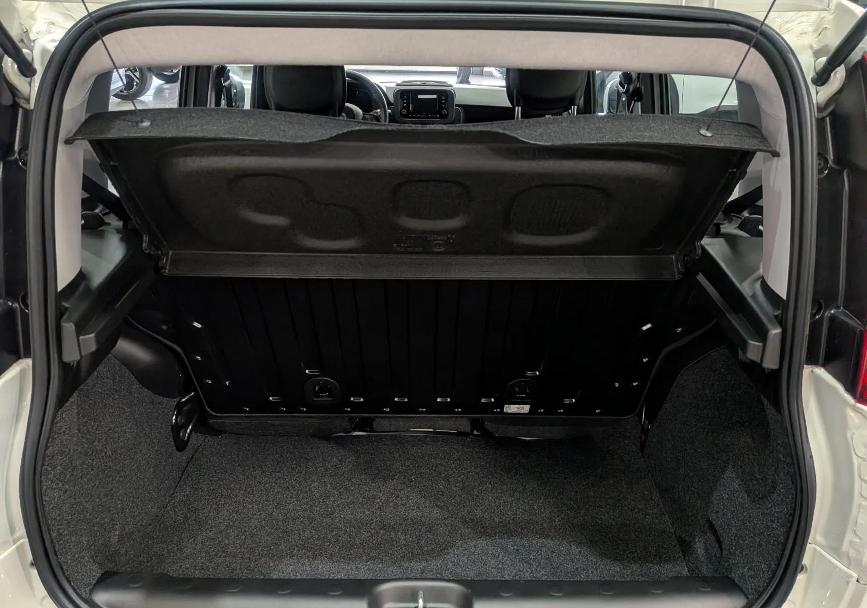 Vue intérieure du coffre ouvert d'une FIAT PANDA 1.0 70 CH HYBRID CITY blanc Gelato, montrant la banquette arrière et le tableau de bord.