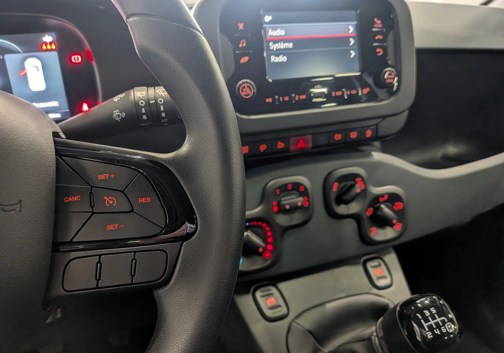 Vue intérieure centrée sur le volant et la console centrale de la Fiat Panda 1.0 Hybrid 2025 avec boîte manuelle et commandes éclairées rouges.