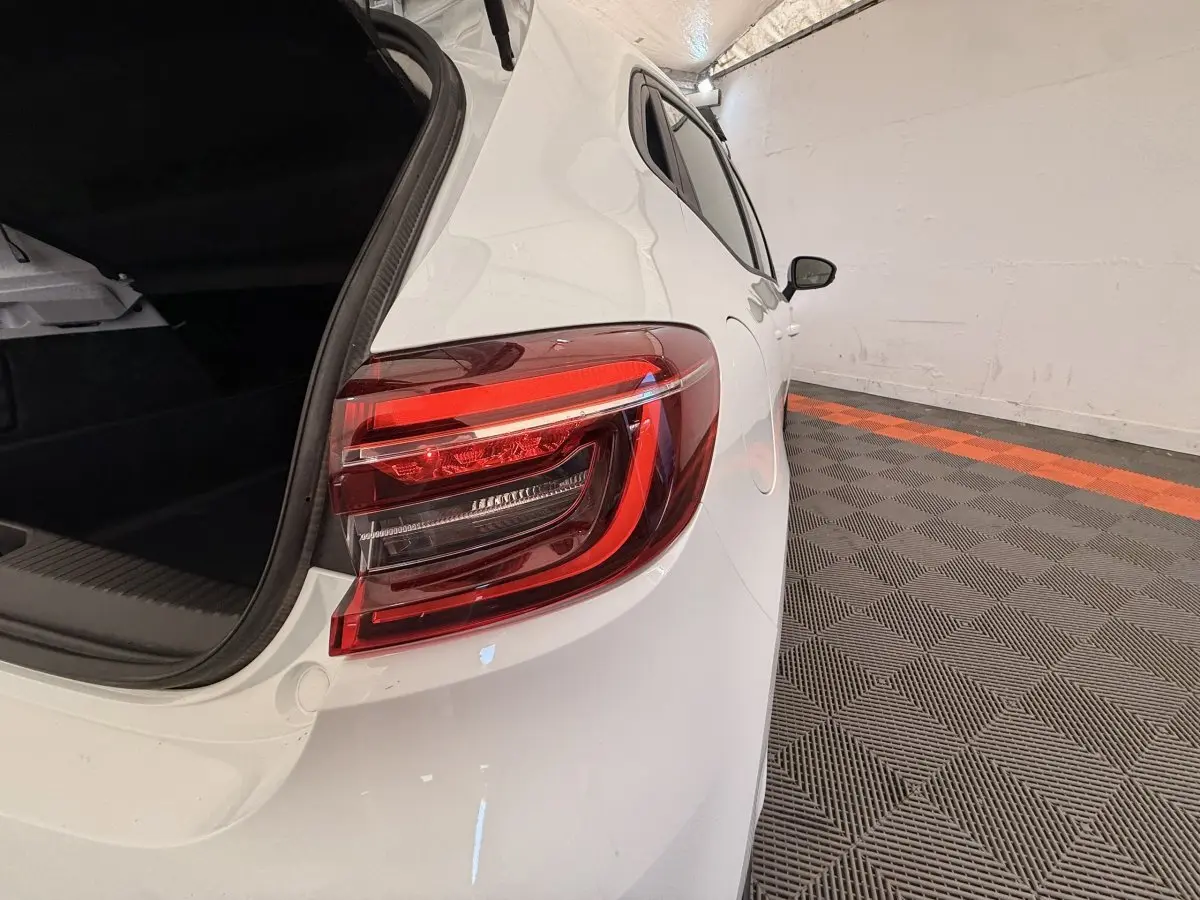 Vue arrière côté droit d'une Renault Clio blanche 2022 avec coffre ouvert et feux arrière LED visibles.