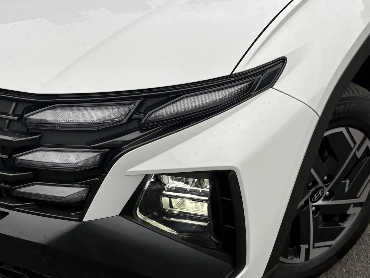 Gros plan sur l'avant droit blanc Atlas du Hyundai Tucson 2026, mettant en valeur les phares bi-LED et la jante alliage.