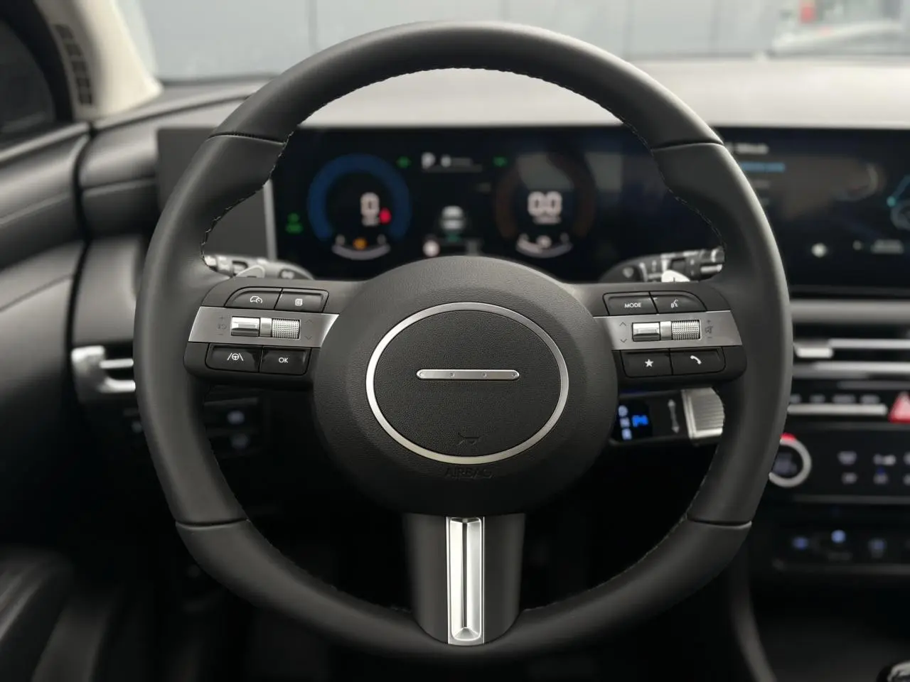 Vue rapprochée du volant noir du Hyundai Tucson 2026 avec commandes intégrées et tableau de bord numérique flou en arrière-plan.