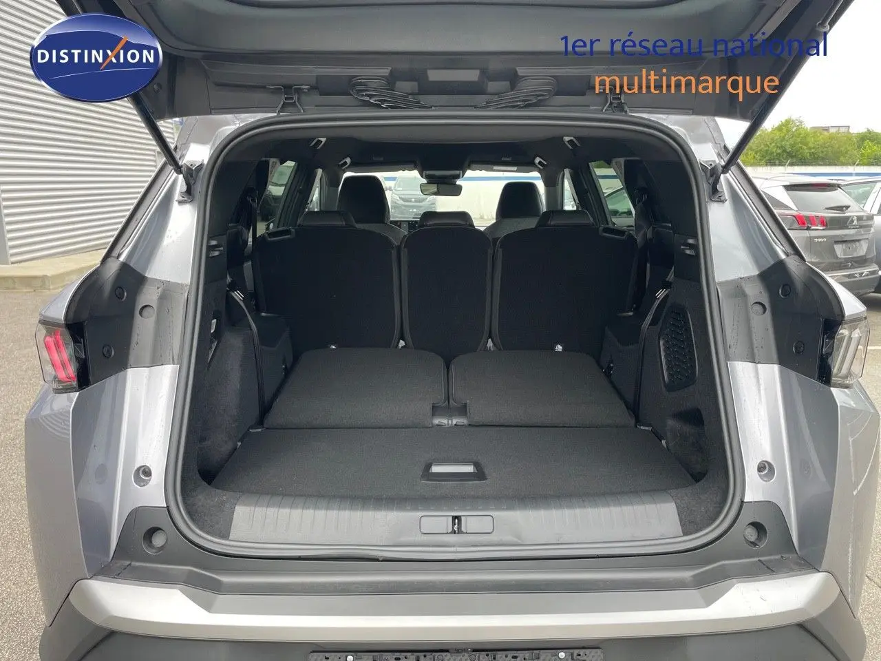 Coffre ouvert vu de l'arrière d'un Peugeot 5008 gris Artense, sièges arrière rabattus pour un grand espace de chargement.